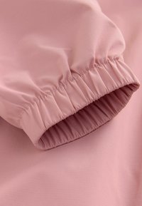 Nahaufnahme eines pinken Stoffärmel mit elastischem Bündchen und subtiler Netzstruktur auf dem Material.