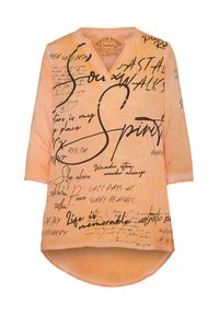 Pfirsichfarbene Bluse mit V-Ausschnitt, Dreiviertelärmeln und abgerundetem Saum. Verfügt über schwarze und goldene Schriftzüge sowie abstrakte Muster auf dem Stoff.