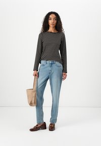 Stripete langermet topp, svart og kremfarget; lyseblå høyt midje denim jeans; brune loafers med gullakenter; lysebrun veske med håndtak.