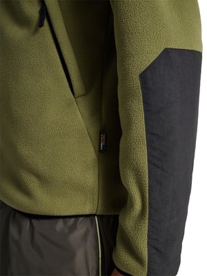 Olivgrüne Fleecejacke mit schwarzem verstärktem Stoffflicken am Ärmel und einem kleinen Cordura-Stoffetikett nahe der Tasche.
