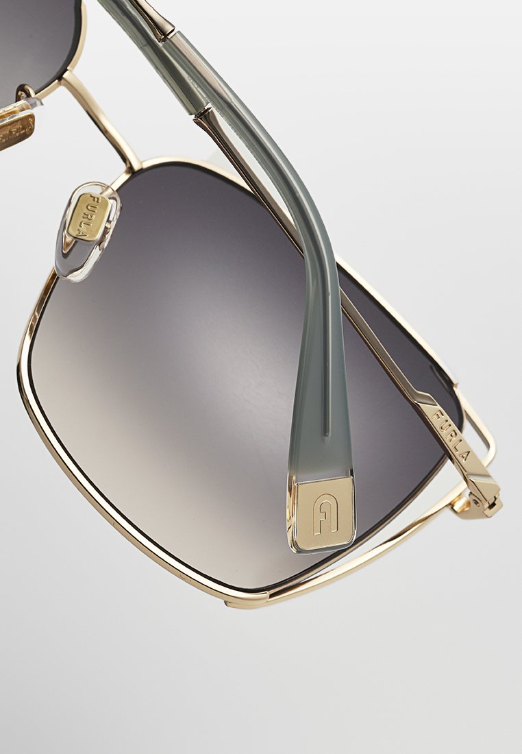 Gafas de sol en tono dorado con un gran marco geométrico, lentes degradados y patillas de color verde claro. Presentan un acento de logo dorado en la varilla.