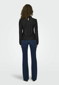 Black long-sleeve blouse with textured fabric, featuring puffed shoulders and back keyhole opening, paired with flared blue jeans.