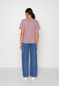 T-shirt mauve a maniche corte e vestibilità rilassata abbinato a jeans blu a vita alta, di media tonalità, con tasche laterali e orlo risvoltato.