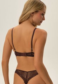 Bra und Tanga-Set aus brauner Spitze mit verstellbaren Trägern, gewellten Kanten und einem Haken- und Ösenverschluss auf der Rückseite mit dekorativen Metallteilen.