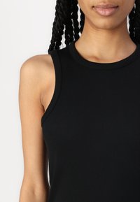 Svart ribbestrikket tank topp med en tettsittende design, rund hals og brede skulderstropper, som fremhever kroppens form og tekstur.
