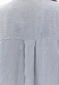 Camicia a righe caratterizzata da linee verticali blu e bianche, yoke arrotondato, dettaglio con piega posteriore e una texture in tessuto leggero.