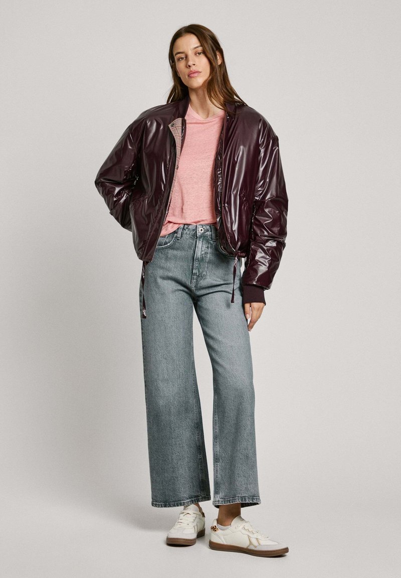 Glänzende burdeos Bomberjacke, hellrosa Rundhals-T-Shirt, hochgeschnittene hellblaue weite Jeans und weiße Sneakers mit braunen Akzenten.