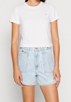 Camiseta blanca de algodón con mangas cortas y cuello redondo, combinada con pantalones cortos vaqueros de color azul claro de talle alto que cuentan con dos bolsillos frontales.