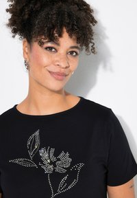 Camiseta negra con un diseño floral hecho de Strass, de manga corta y con cuello redondo, sobre un fondo claro.