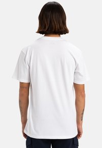 Camiseta de algodón blanca con cuello redondo y mangas cortas, que presenta un dobladillo recto y un logo sutil en la parte superior de la espalda.