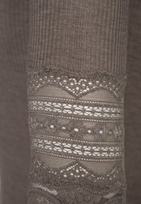 Sivi pleteni tekstil s rebrastom teksturom i složenim čipkastim detaljima sa valovitim rubovima. Uzorci uključuju cvjetne i geometrijske motive.