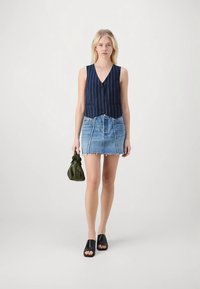 Navy pinstriped sleeveless vest, blue denim mini skirt with frayed hem, black slide sandals, and a green drawstring bag.