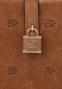 Brązowa skórzana torba o gładkiej fakturze, z dodatkiem złotego zamka na kłódkę i tłoczonym logo. Prostokątny kształt z eleganckim paskiem.