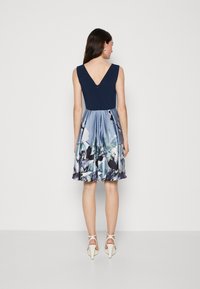A sleeveless dress with a fitted navy top and a flared satin skirt featuring floral patterns in shades of blue and green. V-back detail.