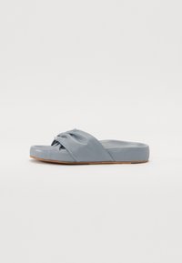 Sandale à glissière en matériau bleu doux avec un design de sangle nouée. Présente une semelle basses et une surface lisse, idéale pour une tenue décontractée.