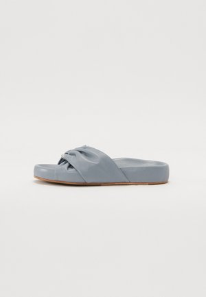 Sandale à glissière en matériau bleu doux avec un design de sangle nouée. Présente une semelle basses et une surface lisse, idéale pour une tenue décontractée.