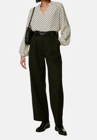 Hvid bluse med sorte prikker, ballonærmer og V-hals, parret med højtaljede sorte bukser og ankelstøvler. Sort crossbody taske.
