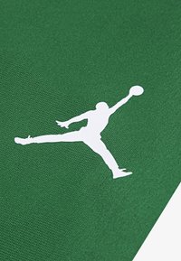 Tela verde con una superficie texturizada, adornada con la silueta blanca de una figura en salto sosteniendo una pelota de baloncesto.
