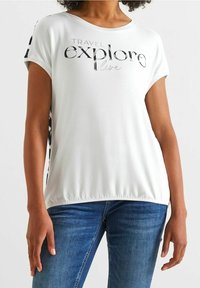Bílý tričko s krátkým rukávem s nápisem "Cestuj, objevuj, žij". Má černobílé vzorované akcenty na bocích. Měkká, elastická tkanina.