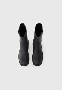 Botas de cuero negro hasta el tobillo con una textura suave, punta redondeada y detalle de hebilla lateral. Diseñadas con un tacón bajo de bloque.