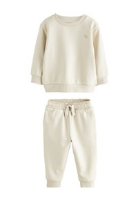 Heledat beež värvi pusa soonikkoes varrukate ja äärega, mida on kombineeritud sobivate kitsenevate pükstega, mis on elastse vöö ja taskutega.