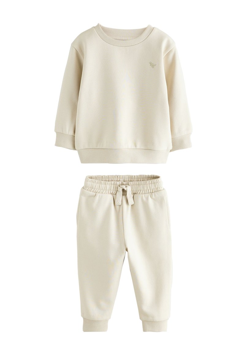 Heledat beež värvi pusa soonikkoes varrukate ja äärega, mida on kombineeritud sobivate kitsenevate pükstega, mis on elastse vöö ja taskutega.