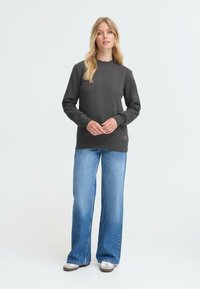 Mørkegrå hettegenser med lange ermer og rund hals, kombinert med lyseblå vide jeans. Har en diskret logodetalj.