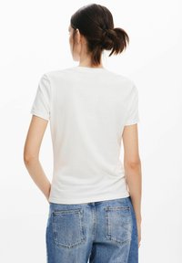 T-shirt bianco in cotone con una silhouette aderente e maniche corte. Il retro presenta un design semplice senza motivi o accenti visibili.