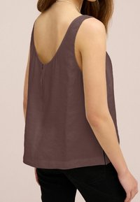 Haut marron sans manches avec un dos décolleté, doté d'une fermeture à glissière et d'un tissu doux légèrement texturé. L'ourlet se situe au niveau des hanches.