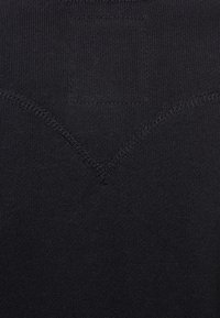 Schwarzer Stretchstoff mit glatter Textur und einem V-förmigen Nahtdetail. Keine weiteren Muster oder Hardware sichtbar.