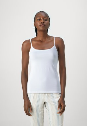 Weißes ärmelloses Top mit quadratischem Ausschnitt, aus glattem Stoff. Das Modell trägt gestreifte Hosen in Blau- und Cremetönen.