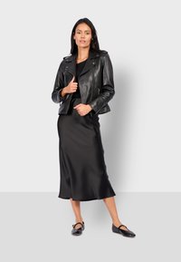 Černá kožená motocyklová bunda přes černé saténové midi šaty. Šaty mají volný spodní lem. Černé ploché boty se zdobnou sponou završují outfit.