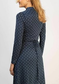 Mekko pitkillä hihoilla tummansinisestä kankaasta, jossa on valkoinen abstrakti kuvio. Mekko on vartalonmyötäinen ja siinä on säädettävä nyöri takana.