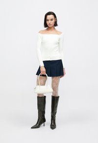 Bel beli pulover z rebrastim vzorcem brez ramen, mornarsko modra mini krilo z volani, vzorčaste prosojne nogavice, črni škornji s peto do kolen, bela torbica z ukrivljenimi ročaji.