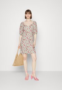 Vestido florido com mangas bufantes, fundo branco, flores em tons de rosa e verde. Combinado com uma bolsa tote de palha e sandálias de salto alto rosa com tiras.