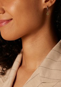 Silberner Creolenohrring mit einem kleinen gelben Edelstein. Glattes Metall mit polierter Oberfläche, hängt knapp unter dem Ohrläppchen.