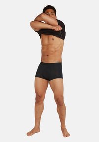 Černé boxerky z jemného materiálu s kontrastním pasem, předváděné na mužské postavě, která zvedá upnuté černé tričko.