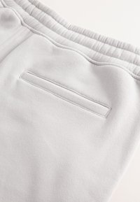 Tissu gris clair en gros plan montrant une ceinture élastique et une unique poche arrière horizontale avec une couture propre.