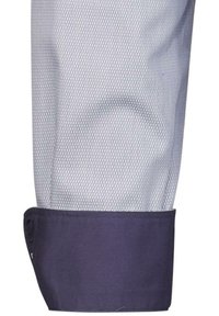 Manica di camicia in rete blu chiaro con polsino blu scuro. Il polsino presenta un design uniforme in contrasto con il materiale testurizzato della manica.