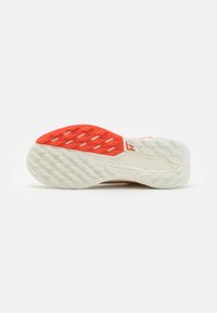Semelle de chaussure avec une base en caoutchouc blanc texturé, accent rouge au niveau du talon et un motif de semelle en zigzag pour l'adhérence. Logo de la marque visible.