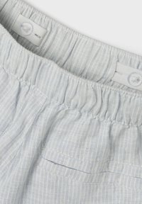 Tissu rayé bleu clair avec une taille décontractée. Présente un bouton et un rassemblement élastique. Poche horizontale sur le côté de la taille.