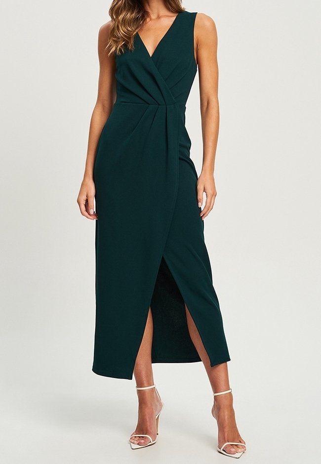 Vestido maxi sin mangas de color verde oscuro con escote en V, detalle de frente retorcido y una abertura lateral. Tejido suave, de largo hasta el tobillo, combinado con tacones de tiras.