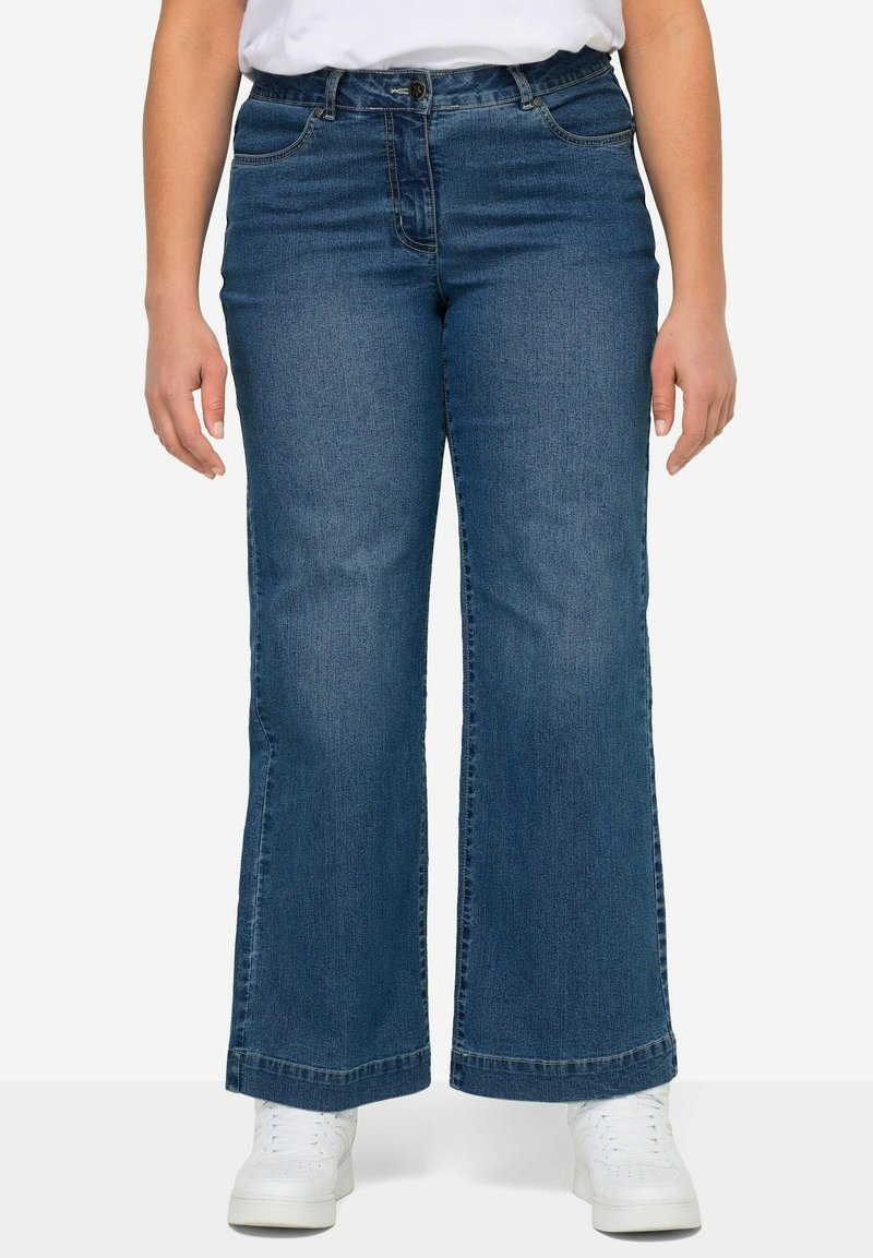Jeans de mezclilla azul oscuro con un corte de pierna ancha, que cuentan con cinco bolsillos, un cierre delantero de botón y un acabado desgastado en las rodillas.