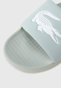 Γαλάζιο λαστιχένιο σανδάλι με υφασμένη σόλα, με λευκό λογότυπο κροκοδείλου στο λουράκι. Λεία επιφάνεια, μινιμαλιστικός σχεδιασμός.