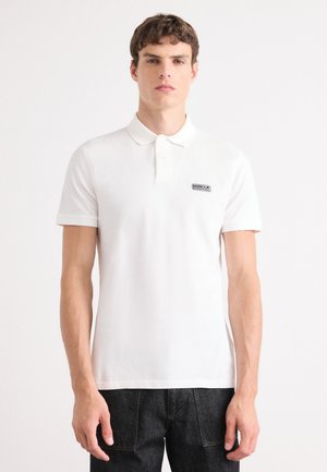 Chemise polo blanche avec un col, des manches courtes et un patch de marque noir sur la poitrine gauche. Fabriquée en tissu texturé.