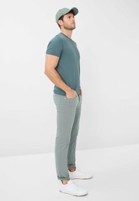 Mintgrünes T-Shirt, hellgrüne Hose und weiße Sneaker. Die Mütze passt zur Farbe des Shirts. Gerade geschnittene Hose mit Taschen, glattes Material.