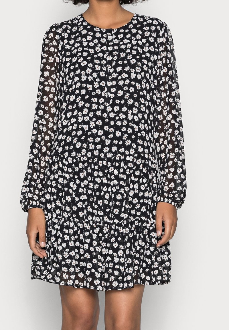 Schwarzes geblümtes Kleid mit langen, transparenten Ärmeln und einem runden Ausschnitt. Verfügt über einen gestuften, gerafften Saum und ein Muster aus kleinen weißen Blumen.