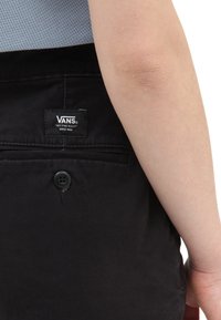 Los chinos negros de Vans cuentan con un bolsillo trasero que presenta una etiqueta negra con el logo de la marca y un cierre de botón negro en el bolsillo.