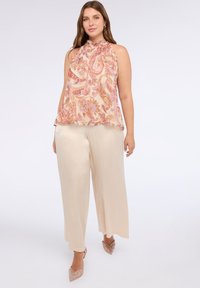 Top halter crema con un motivo paisley rosa e arancione, abbinato a pantaloni beige larghi e tacchi nude glitterati.