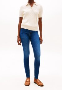 Vitt kortärmat kabelstickat tröja med krage, blå skinny jeans och bruna loafers med en dekorativ kedjeaccent.